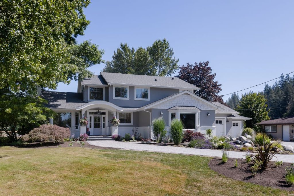 Front view of a bright, coastal-inspired family home with soft natural tones, set against a country meadow backdrop, blending timeless design with playful, family-friendly charm.